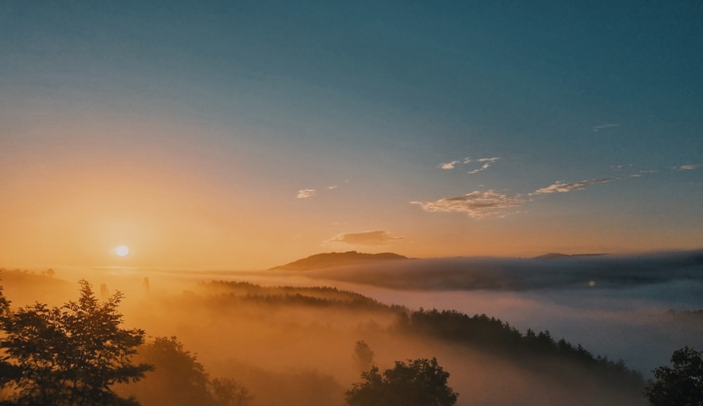 the sun is setting over a foggy valley