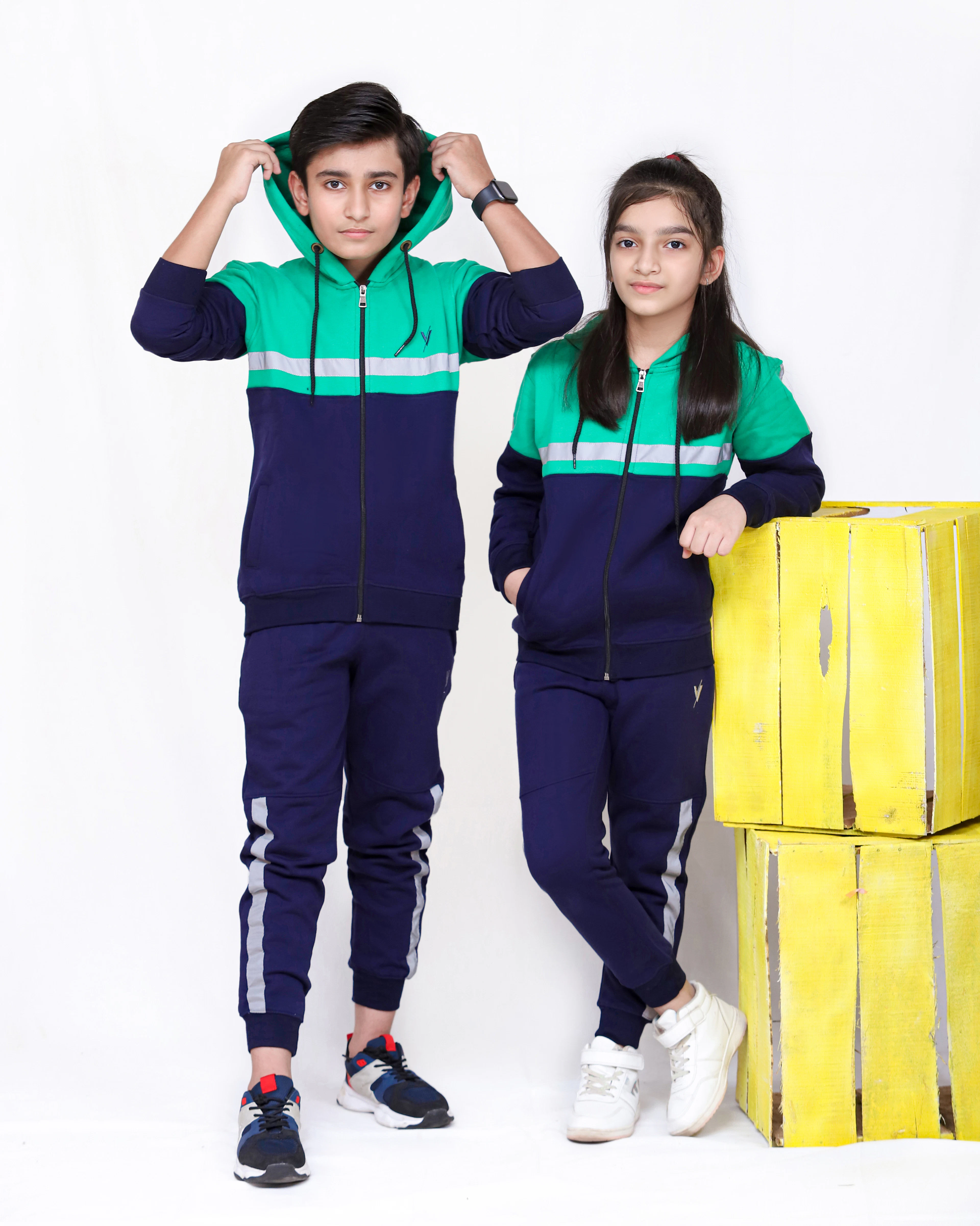 Two kids in matching navy and green colour-block tracksuits