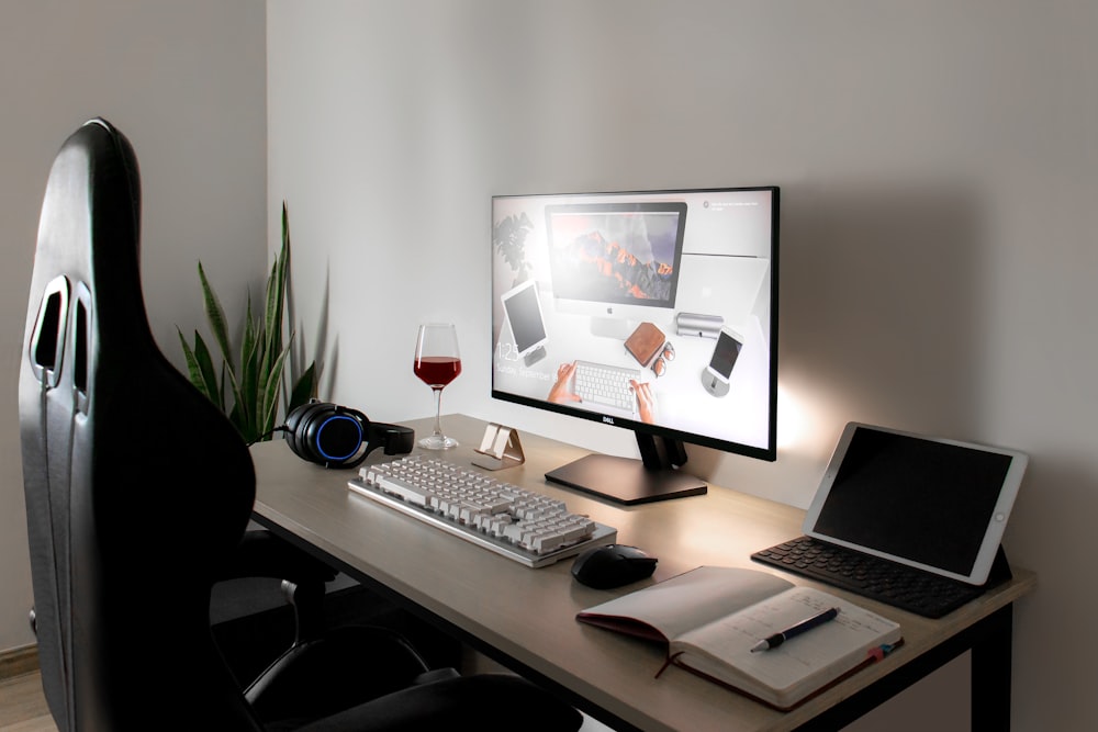 a desk with a computer, keyboard, mouse and a glass of wine