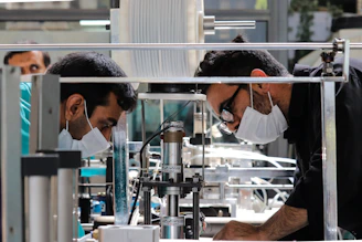 two men in masks working on a machine