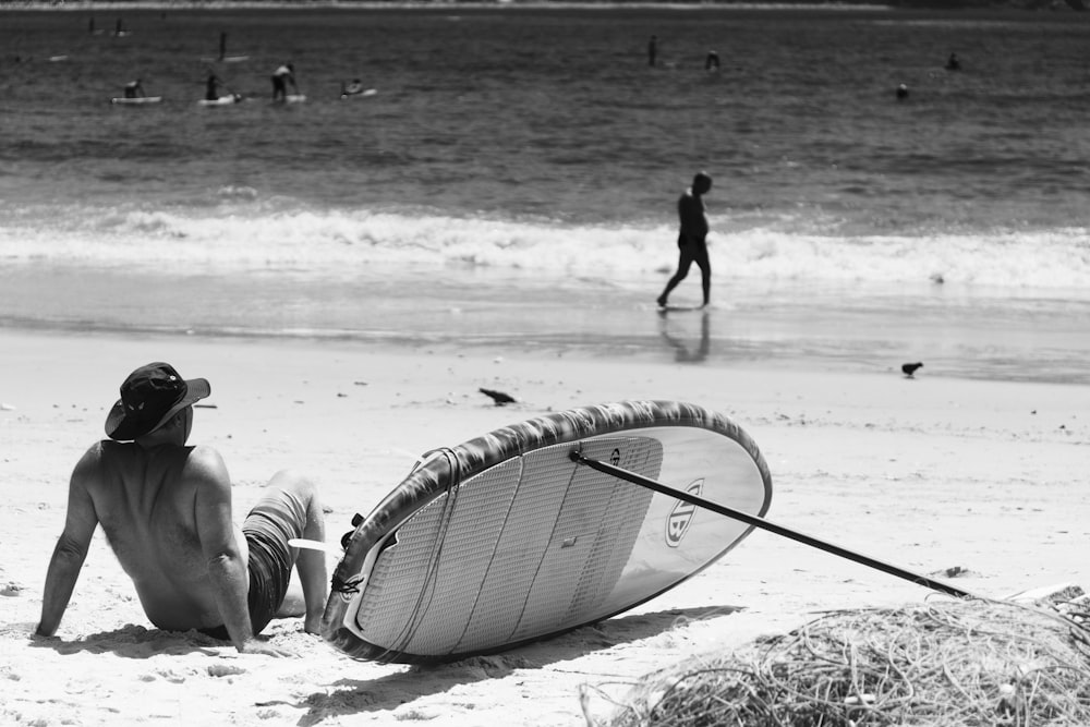 a man sitting on a beach next to a surfboard