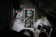 A close-up photograph of a printed image featuring a child in camouflage attire holding a toy gun, situated among other photographs. One noticeable item is a camera positioned at the bottom right corner.