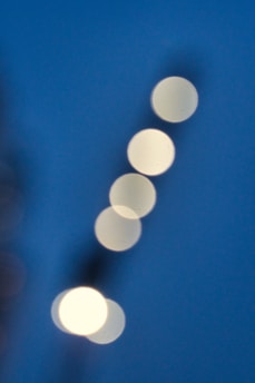 Five circular, white light orbs are arranged diagonally against a deep blue background. The image has a soft focus, creating a dreamy and abstract appearance.