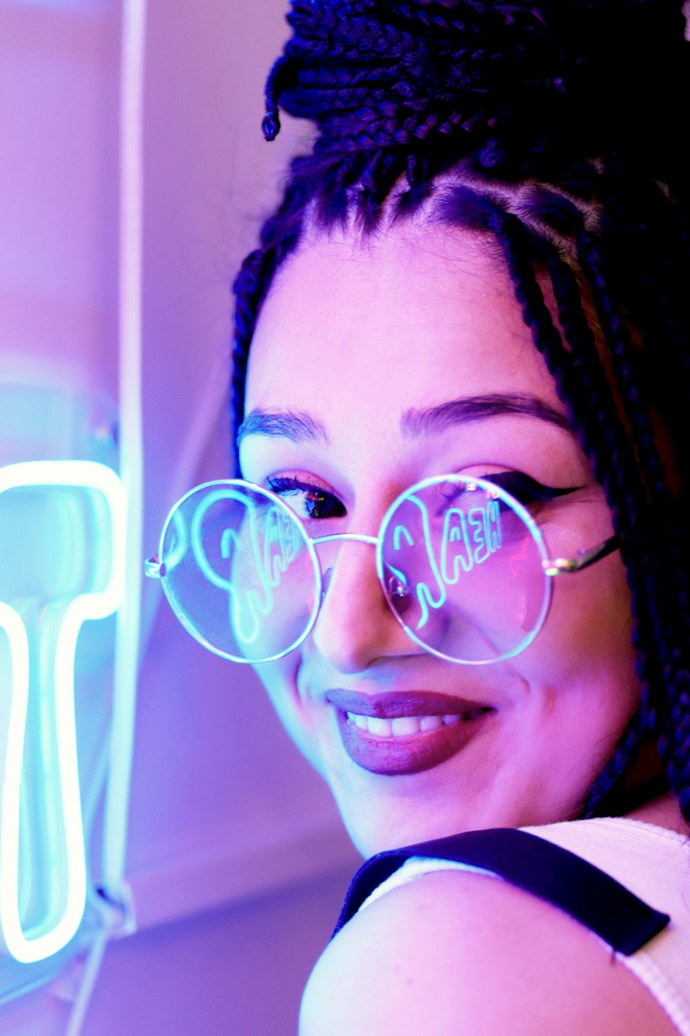 a woman wearing glasses and smiling in front of a neon sign