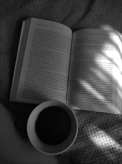 A close-up of a black and white coffee cup beside an open ebook, with soft natural light casting shadows.