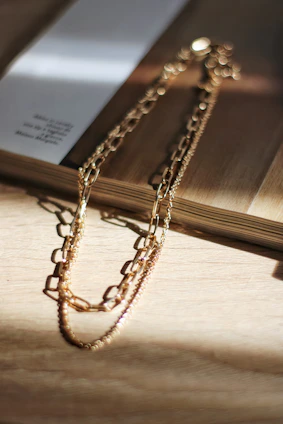Close-up of a delicate gold necklace resting on smooth white fabric, bathed in soft natural light.