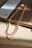 Close-up of a delicate silver leg chain resting on a sunlit wooden table.