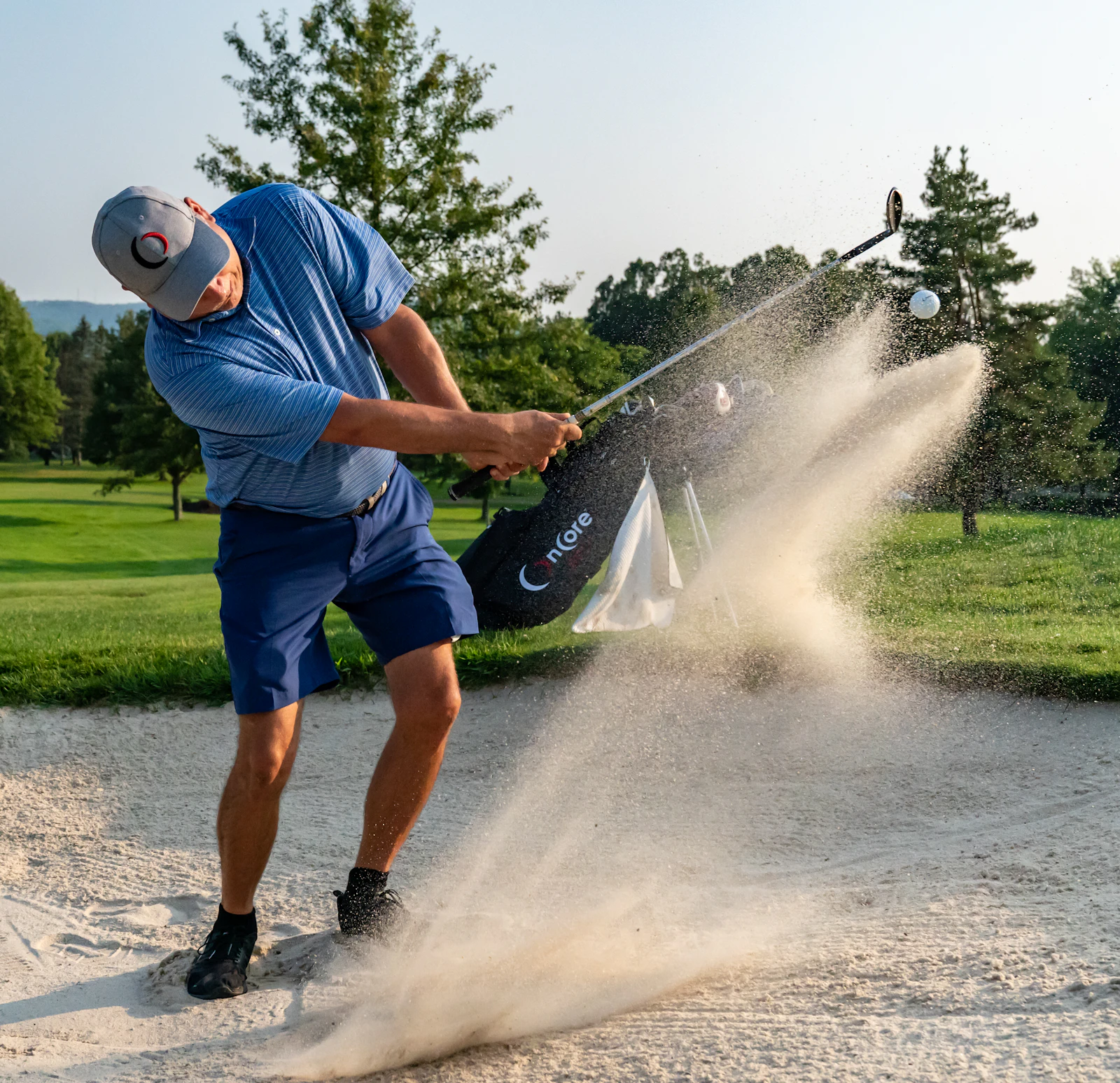 A golfer sends up a spray of sand as he plays a shot from a bunker