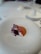 A culinary dish features a delicately plated piece of lobster accompanied by artistic garnishes, including vibrant red leaves and a subtle sauce on a white plate. The setting is minimalist and elegant, suggesting a fine dining experience.