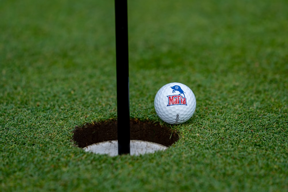 une balle de golf posée au sommet d’un trou dans l’herbe