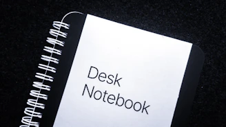 A close-up of a black and red notebook with the title 'b p d unboxed' handwritten on the cover, resting on a dark wooden desk.