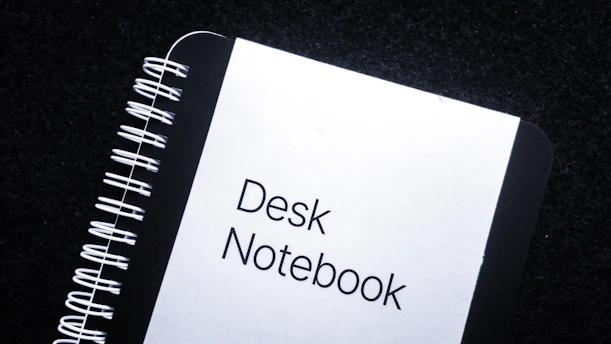 A close-up of a black and red notebook with the title 'b p d unboxed' handwritten on the cover, resting on a dark wooden desk.