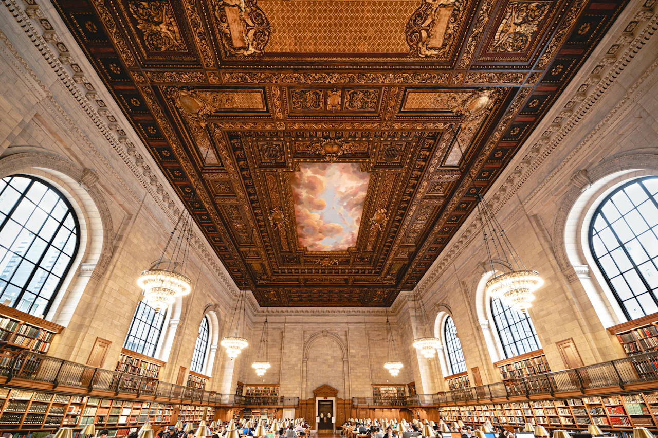 A grand reading room with a decorated ceiling and rows of reading tables