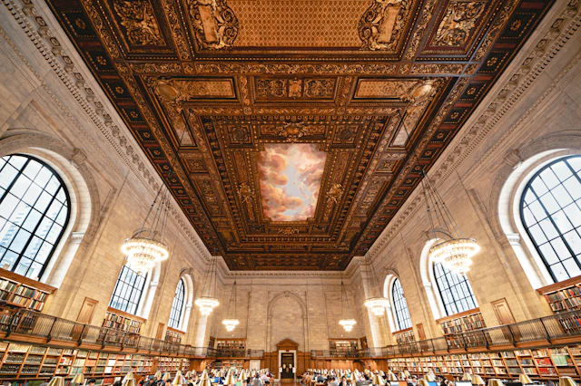 A grand reading room with a decorated ceiling and rows of reading tables