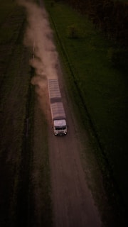 a truck driving down a dirt road next to a lush green field