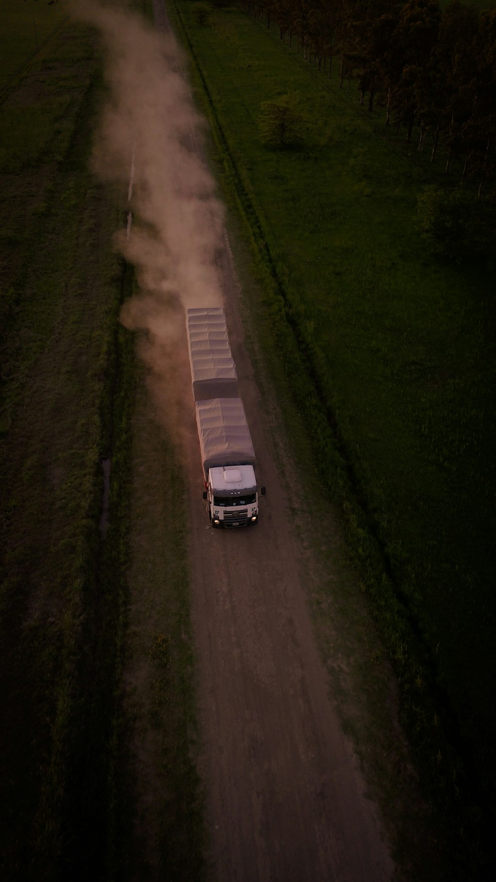 a truck driving down a dirt road next to a lush green field