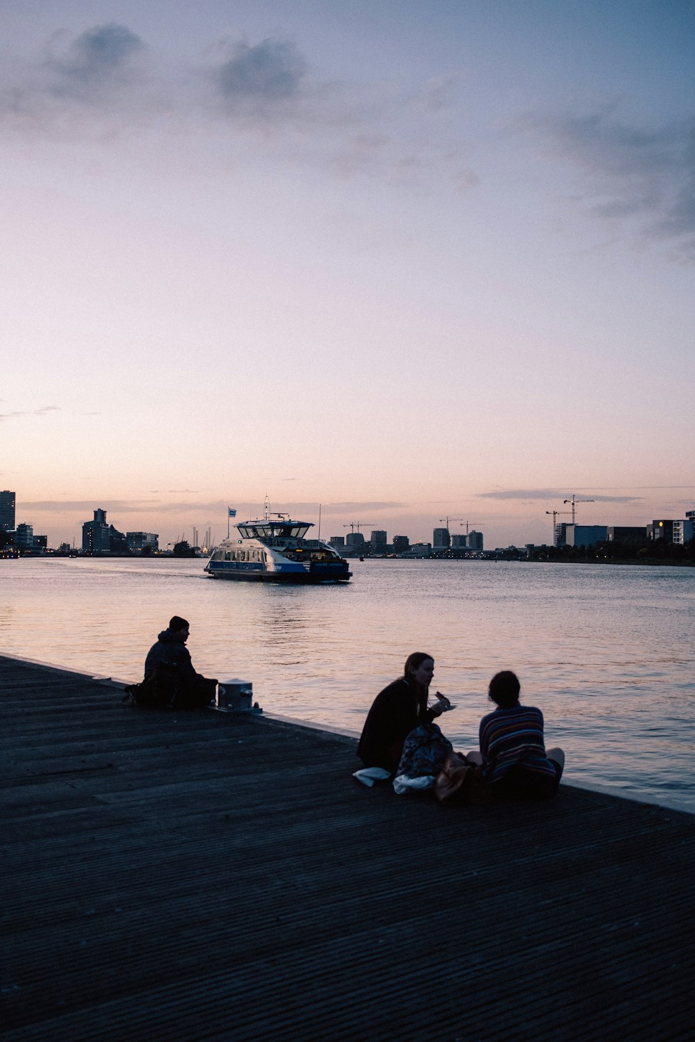 a group of people sitting on a dock next to a body of water