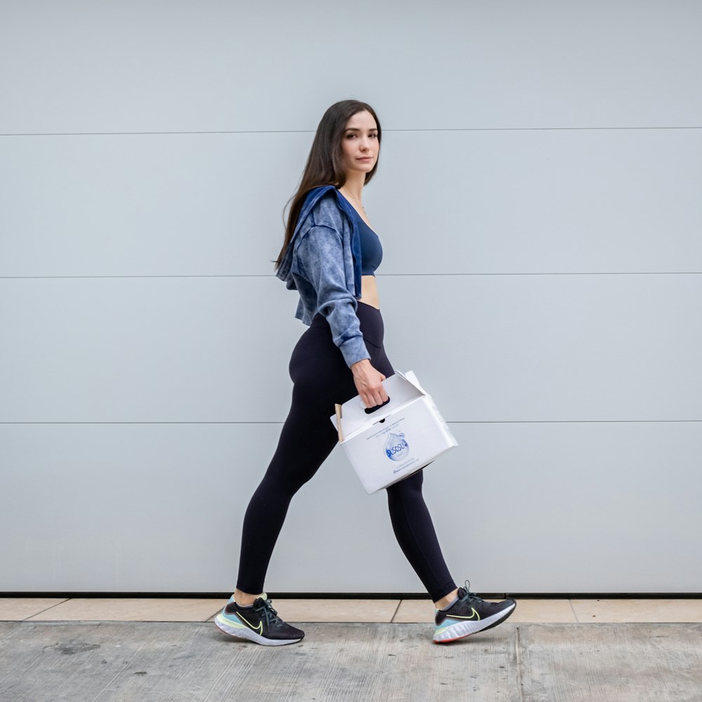 a woman walking down a sidewalk carrying a white bag