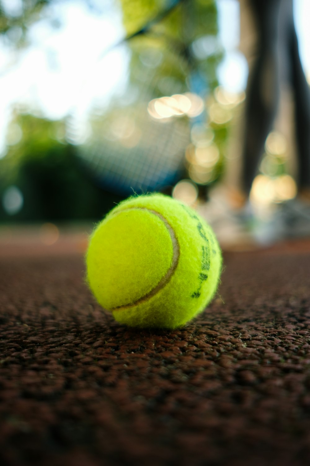 a tennis ball on the ground with a tennis racket in the background