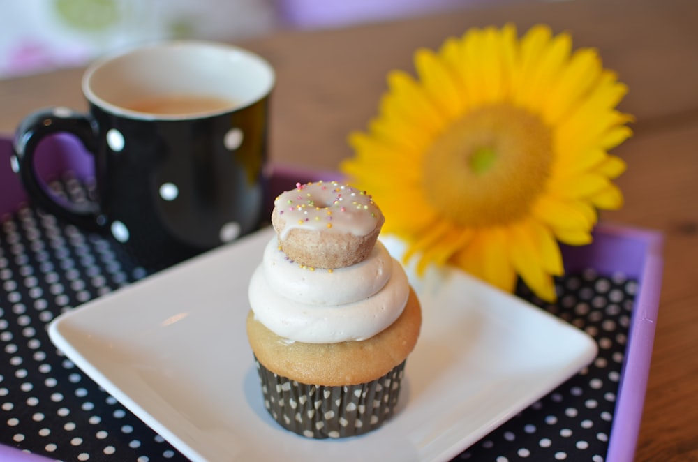 a cupcake sitting on top of a white plate next to a cup of coffee