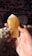 A hand holds a large, translucent crystal with a bright yellow hue. The crystal is faceted, catching the light and revealing internal textures. The background is filled with various other crystals and gemstones, slightly out of focus.