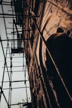 A close-up view of a brick building under renovation, with scaffolding around it. The structure displays intricate architectural details and weathered textures, suggesting age and historical significance.