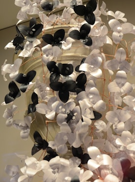 A decorative arrangement featuring white and black paper flowers interconnected by delicate copper wires. The flowers have a three-dimensional appearance, with petals intricately crafted. The background appears neutral, enhancing the prominence of the floral elements.