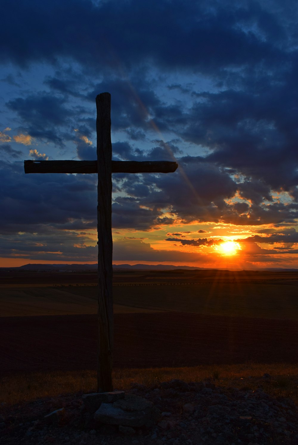 Ein Kreuz auf einem Hügel mit einem Sonnenuntergang im Hintergrund