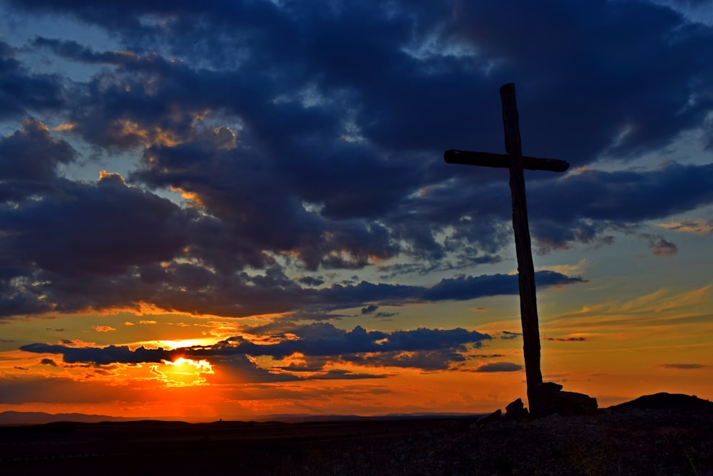 a cross sitting on top of a hill under a cloudy sky