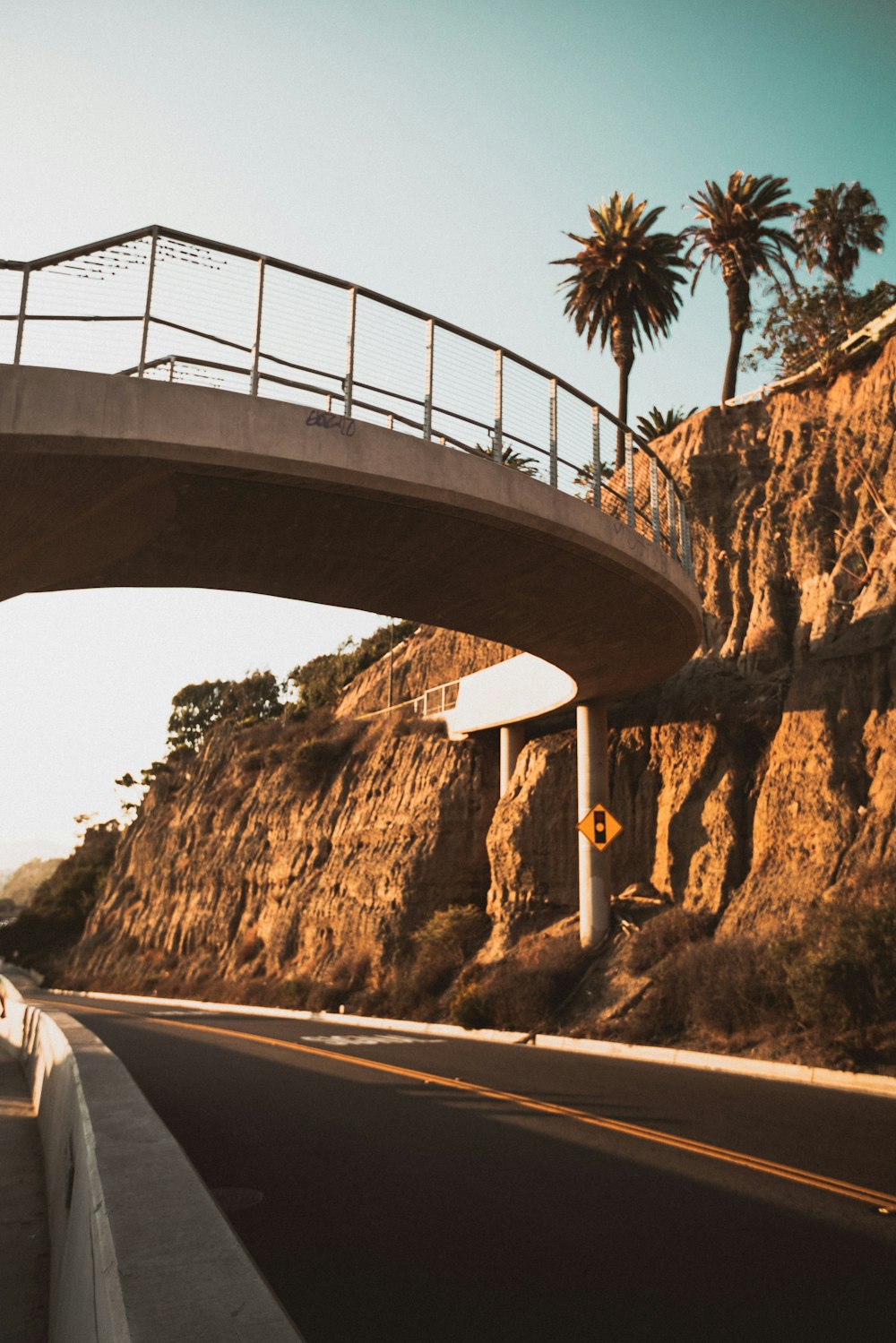 a road with a bridge over it and palm trees on the side of the road