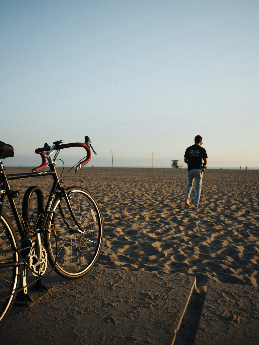 a man walking across a sandy beach next to a bike