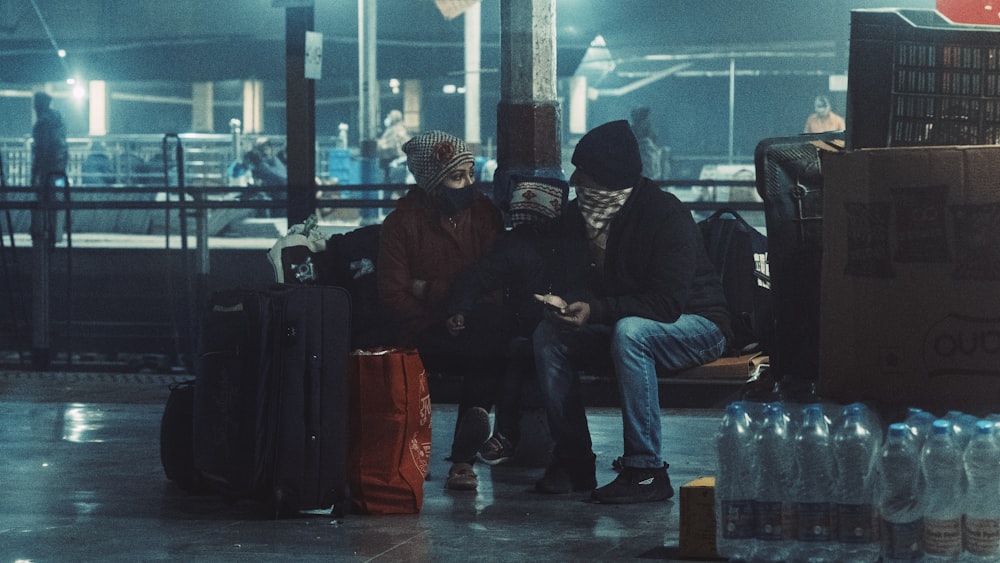 two people sitting on a bench next to luggage