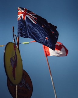 A prominent flag with stars is flying on a clear day alongside another flag in the background. An oval sign with a design is partially visible at the bottom left.