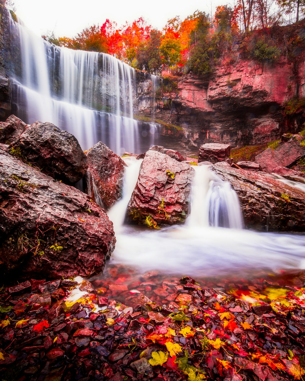 a waterfall with fall leaves on the ground