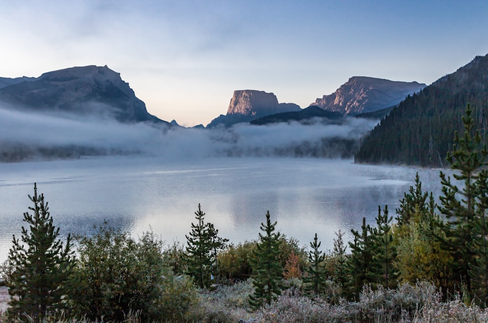 a lake surrounded by trees and mountains covered in fog