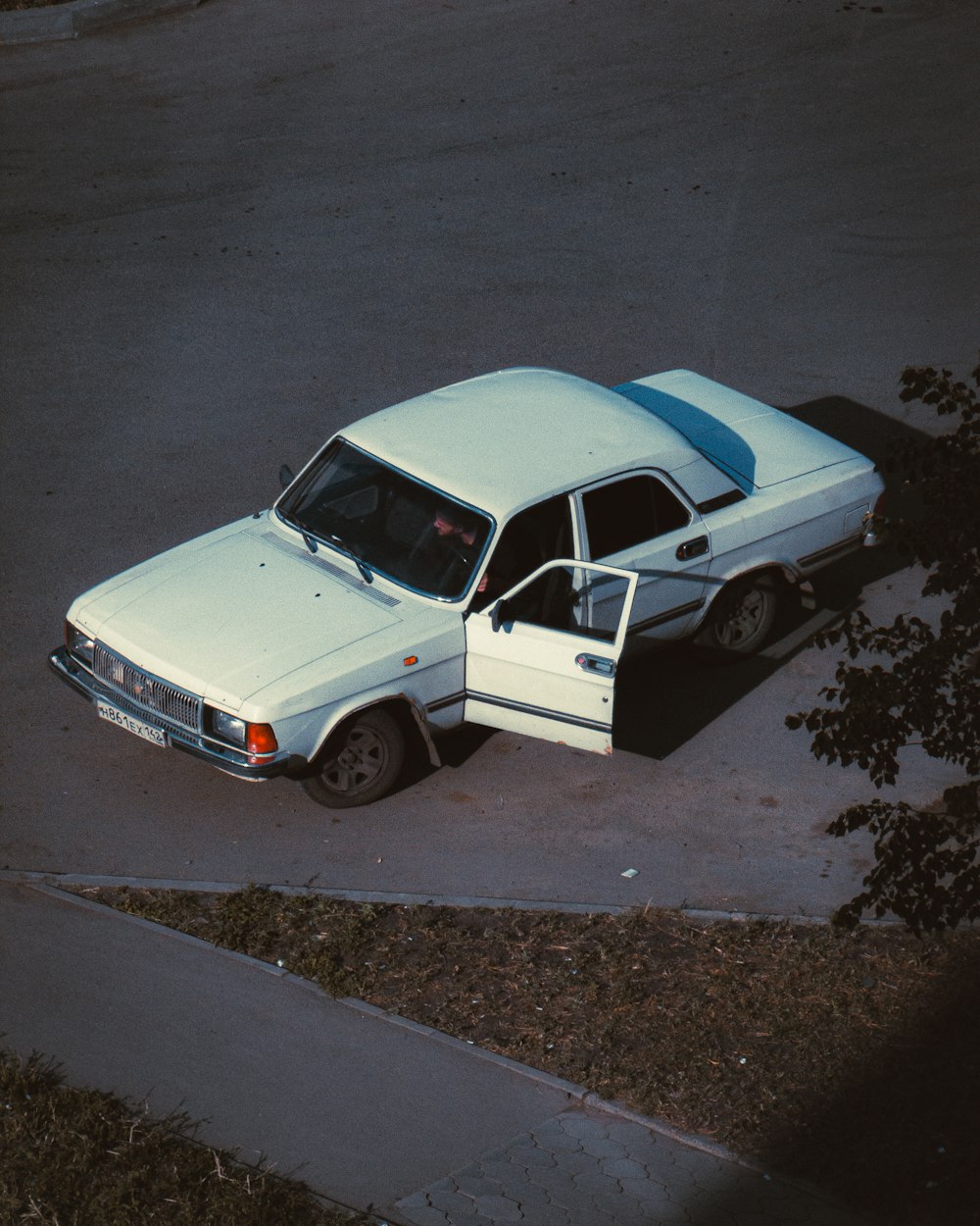 a white car parked in a parking lot next to a tree