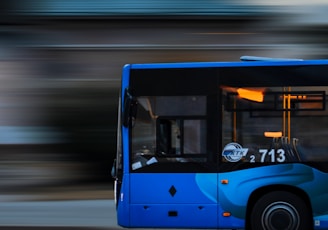 a blue bus driving down a street next to a tall building