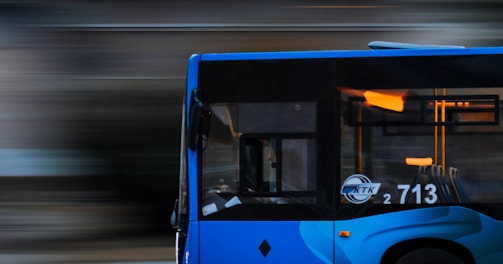 a blue bus driving down a street next to a tall building