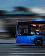 a blue bus driving down a street next to a tall building