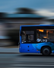 a blue bus driving down a street next to a tall building