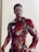 A detailed action figure of a superhero in a red and gold armored suit with intricate designs and glowing elements. The figure has a lifelike appearance, with a serious expression and neatly styled hair. It is positioned upright against a plain background.