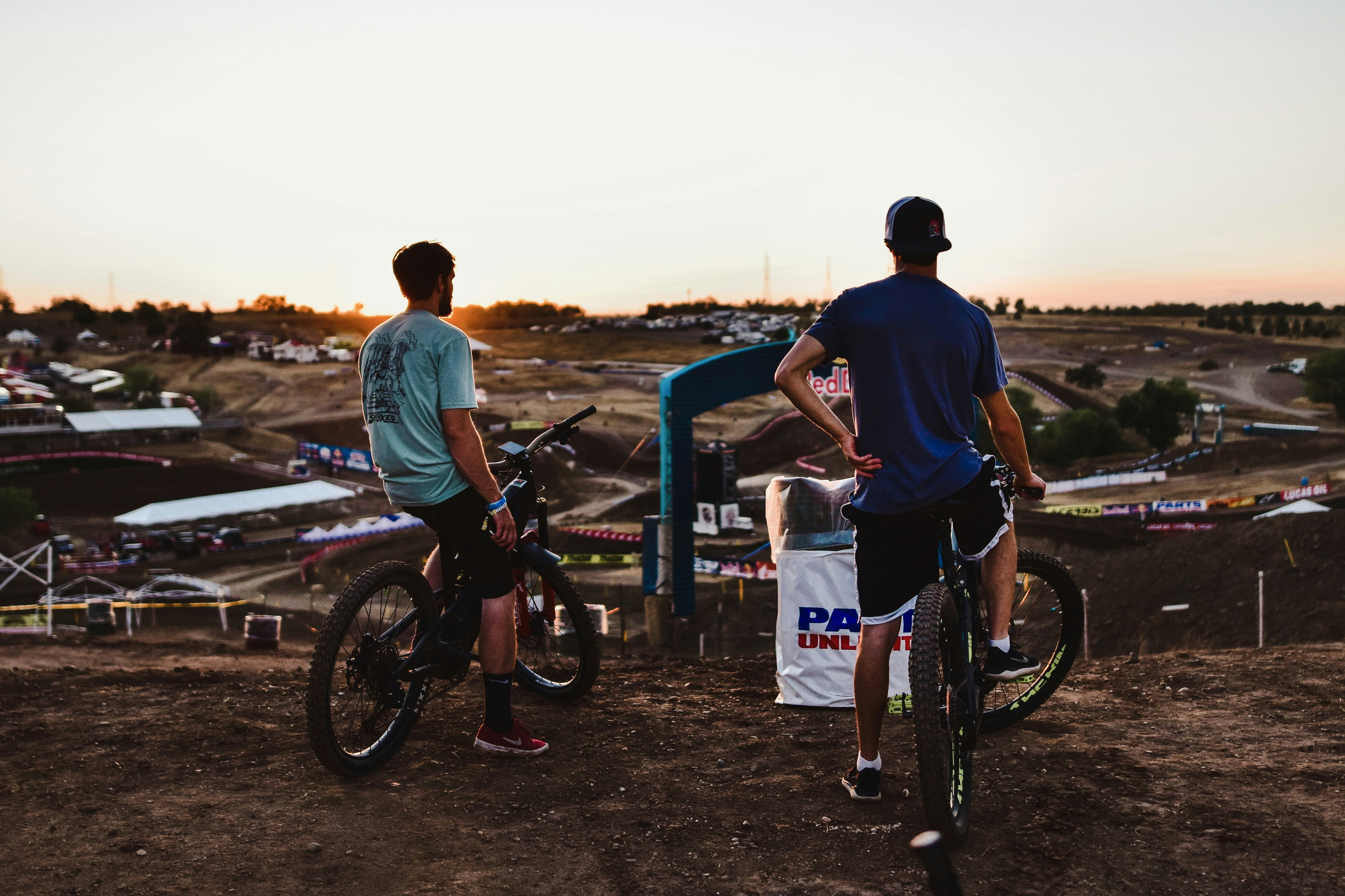 a couple of men standing next to bikes on a dirt field