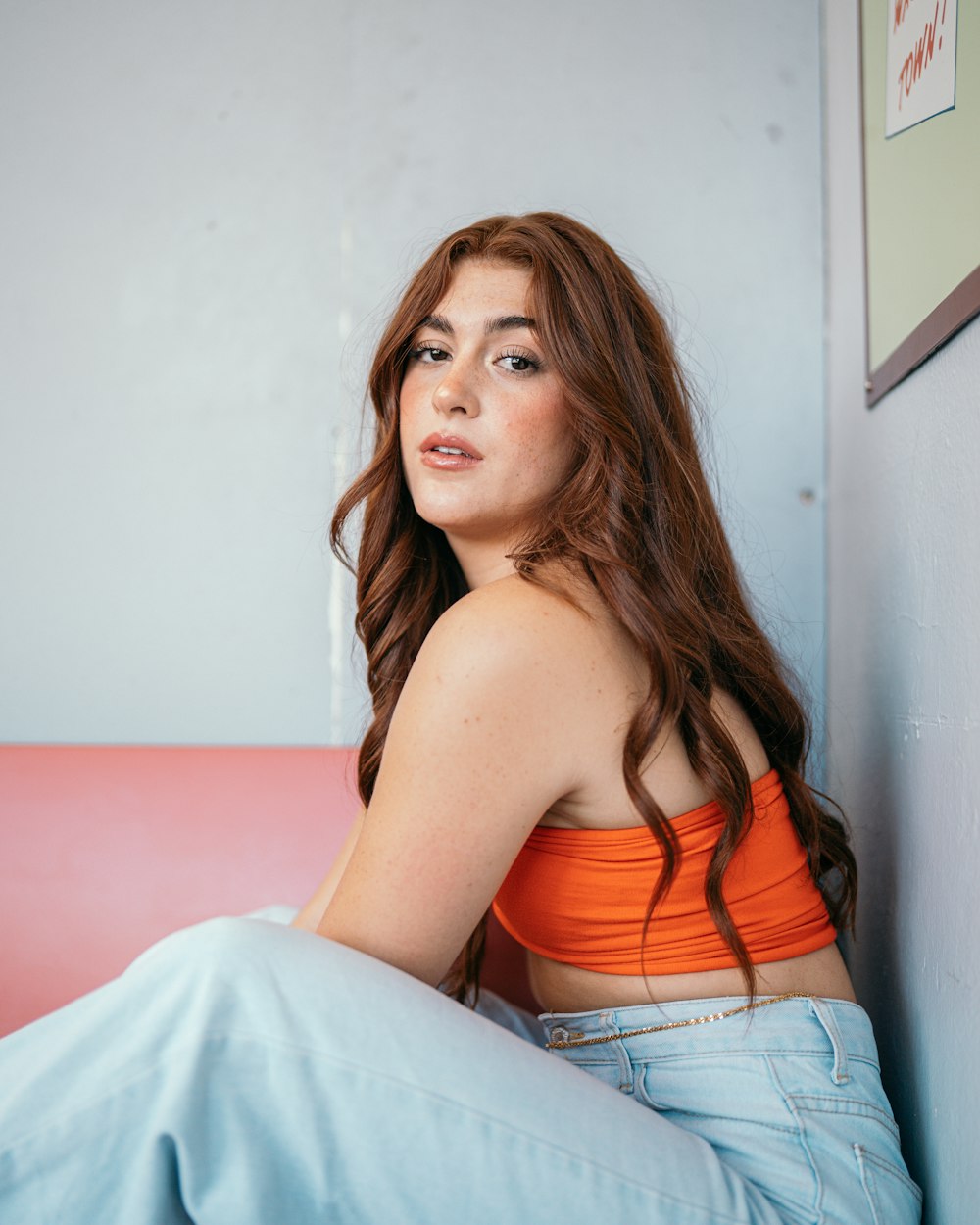 a woman in an orange top sitting on a pink couch