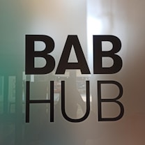 The image features bold black text that reads 'BAB HUB' against a partially reflective glass surface. There is a subtle gradient in the background, transitioning from a greenish hue on the left to a warmer tone on the right. The reflection on the glass suggests a possible indoor environment.