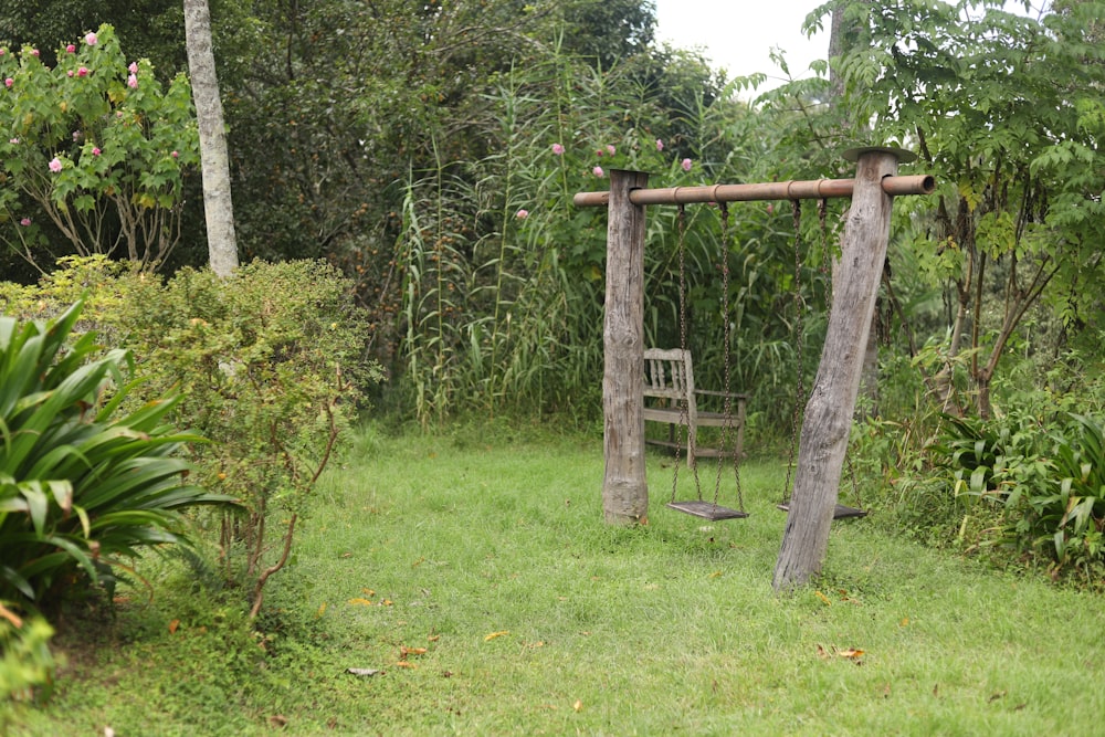 a wooden swing sitting in the middle of a lush green field