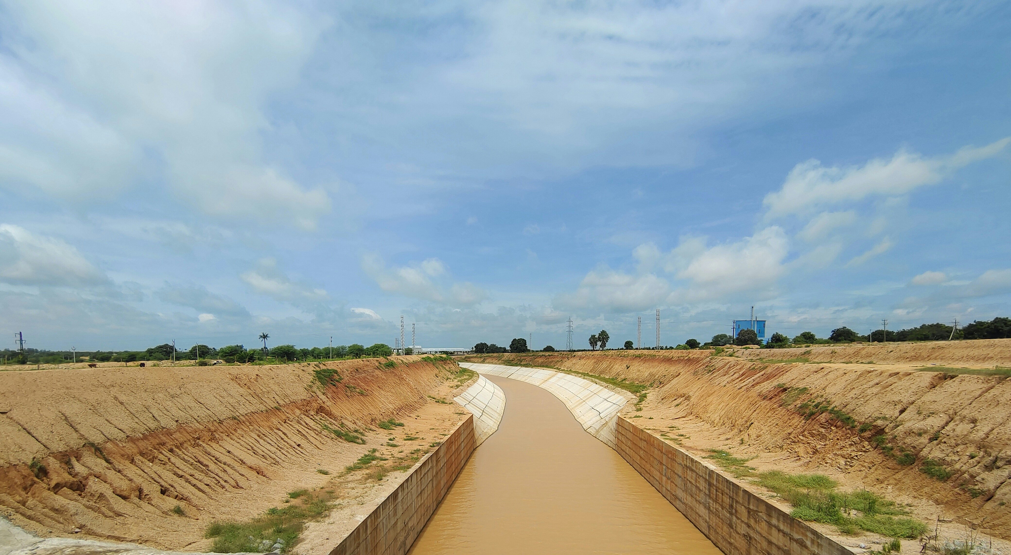 Canal desiltation work with excavator operating in a waterway, murky brown water, earthen banks, overcast West Bengal sky