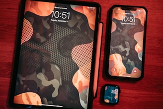 The image features three Apple devices placed on a red wooden surface. A tablet with a stylus attached, a smartphone, and a smartwatch. All devices display a matching abstract camouflage wallpaper with shades of orange, black, and gray, showing the time as 10:51 on the screens.