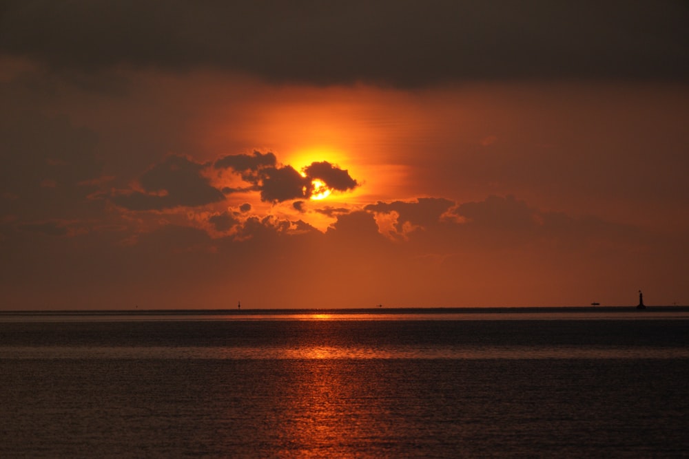 the sun is setting over the ocean with clouds