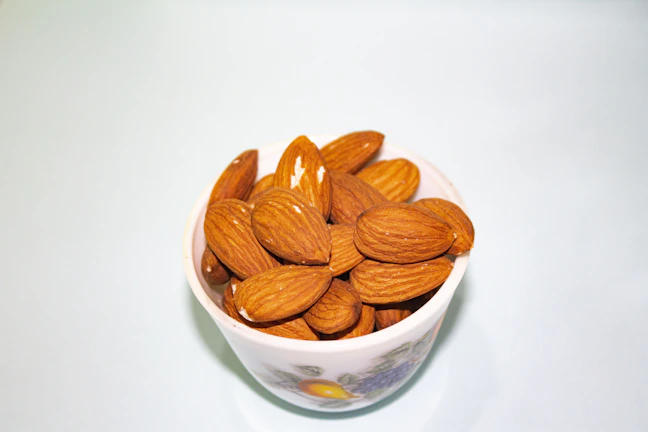 Hands holding a handful of fresh, whole almonds against a white background.