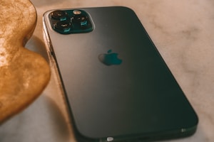 A smartphone with a sleek, dark design is placed on a smooth surface, with its camera lenses prominently visible. The iconic logo is centered on the back. The lighting creates a warm ambiance with shadows and reflections.
